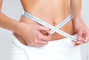 Woman measuring her waist with a tape measure for body contouring treatment.